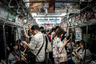 A photograph of people on a public transit train, looking at their phones.