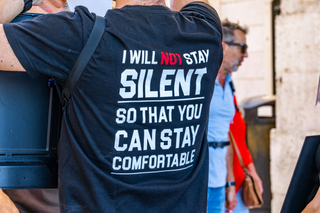 The back of a person's shirt with text that says, "I will not stay silent so that you can stay comfortable."