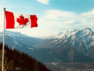 A photo of the Canadian flag against a backdrop of a mountain range.